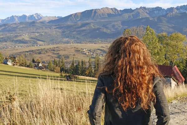 Red-haired woman in a motorcycle jacket is looking at a mountain