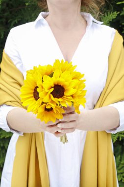 Kadın elinde bir buket ayçiçeği tutuyor..