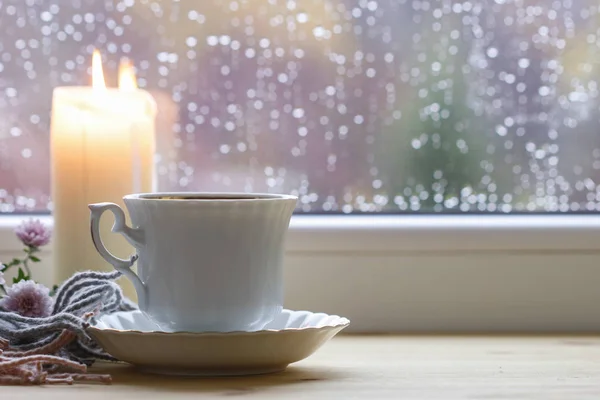 Porzellantasse Tee und eine Kerze am Fenster. — Stockfoto