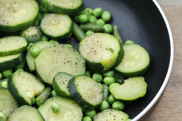 Ervilhas verdes e fatias de abobrinha preparadas para fritar em uma panela . — Fotografia de Stock