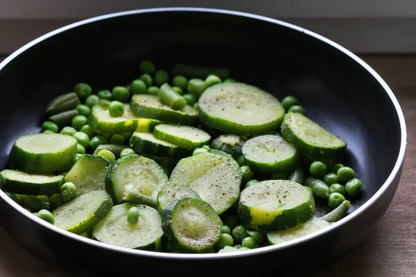 Guisantes verdes y rodajas de calabacín preparados para freír en una sartén . — Foto de Stock