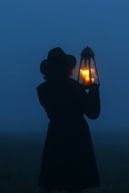 Woman is holding an iron lantern, with candle inside, in her han