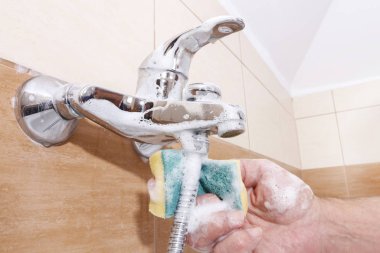 Temizlik işçisi banyo musluğunu temizler..