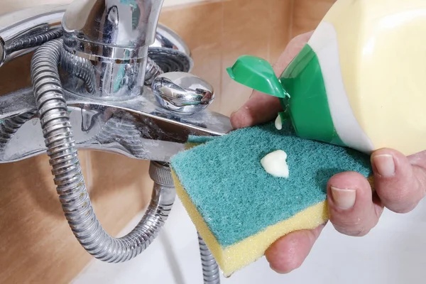 A cleaning service worker cleans a bathroom tap.