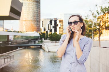 Genç kadın modern binalar ve gölet cep telefonu konuşma yaparken çalışma görevlerini tartışarak duruyor.