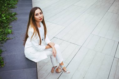 Beyaz elbiseli güzel gülen kadın ofis binası bahçesinde açık havada oturuyor 