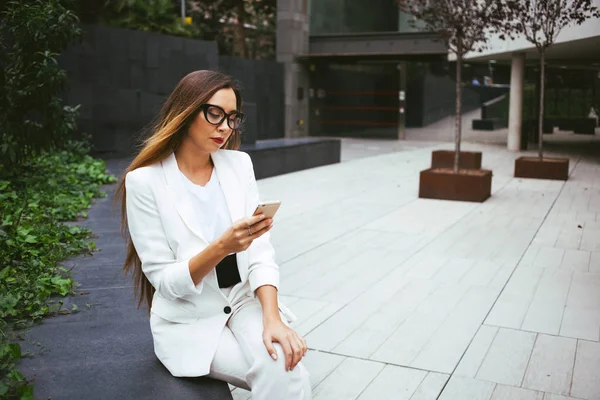 Primer plano retrato de mujer hermosa en traje blanco está sentado al aire libre en un patio trasero y el uso de su teléfono celular — Foto de Stock