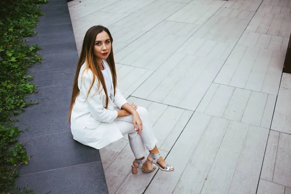 Серьёзная белая деловая женщина в белом костюме сидит на улице во дворе офисного здания — стоковое фото
