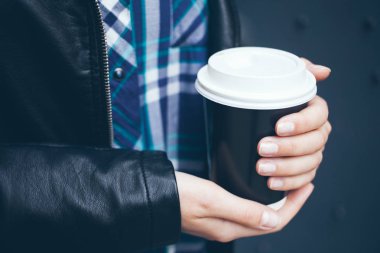 Genç kadın sokakta şehir merkezinde yürürken kahve içiyor.