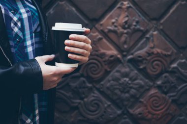 Genç kadın sokakta şehir merkezinde yürürken kahve içiyor.