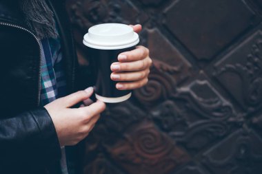 Genç kadın sokakta şehir merkezinde yürürken kahve içiyor.