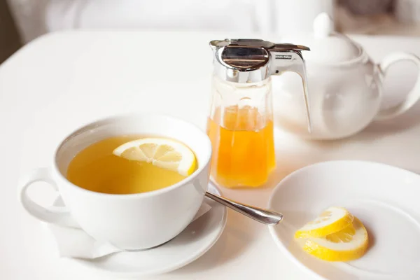 Xícara de chá verde quente com limão na mesa branca, limão fresco e mel - tiro de close-up. Luz solar efeito flair . — Fotografia de Stock