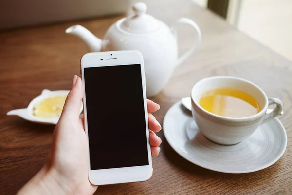 Limonlu çay beyaz fincan, telefon mobil akıllı telefon kadının elini tutuyor.