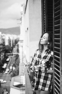 Güzel genç kadın rahatlatıcı kahve ya da çay tutan şehir manzaralı balkon. 