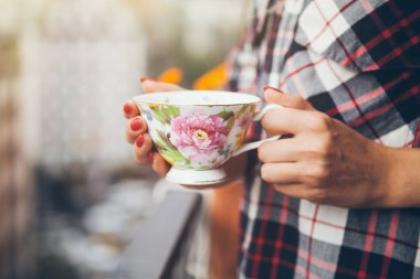 Kadın ekose gömlekli şehir manzaralı bir balkon kahve içiyor.