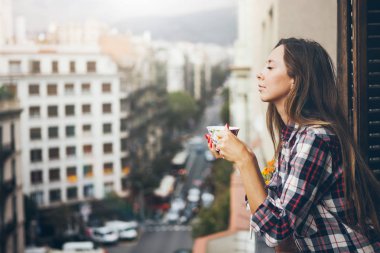 Neşeli genç kız mutlu ve gülümseyen ve içme içmek iştah açıcı kahve fincan yan görünüm