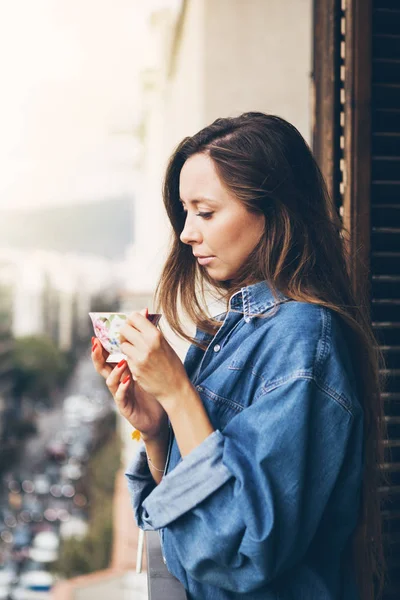 Una hermosa y joven chica caucásica con una camisa vaquera grande sostiene una gran taza de café — Foto de Stock