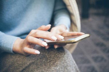 Cep telefonuna mesaj yazan, çevrimiçi iletişimden zevk alan, geri bildirim yapan, mavi kazak giyen beyaz tırnaklı kadınların ellerini kapatın. Teknoloji konsepti