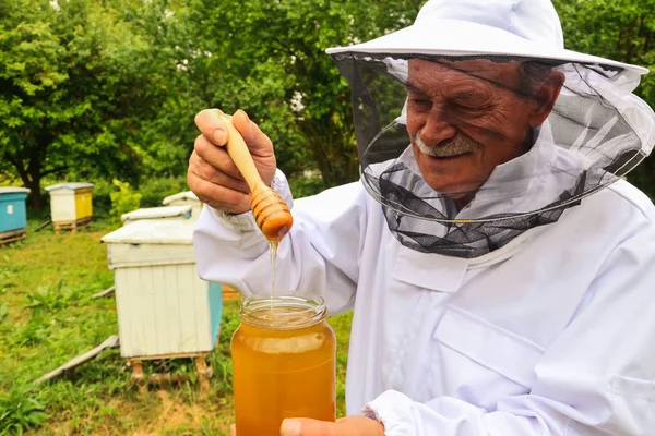 Senior-Imker präsentiert Glas mit frischem Honig im Bienenhaus im Frühling — Stockfoto