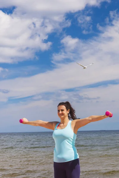 Atractiva joven haciendo ejercicio con mancuernas en una playa en el verano — Foto de Stock