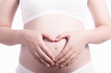 Kadın hamile karnı üzerinde bir kalp şeklinde elele