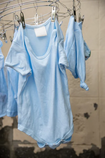 Baby laundry hanging on a clothesline and cement wall — Stock Photo, Image