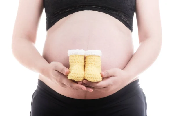 Κλείστε τα μικρά κίτρινα παπούτσια για το αγέννητο μωρό στην κοιλιά της εγκύου — Φωτογραφία Αρχείου