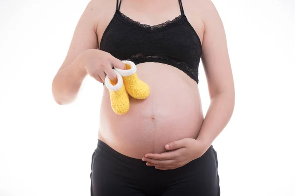 Μικρά κίτρινα παπούτσια για το αγέννητο μωρό στην κοιλιά της εγκύου — Φωτογραφία Αρχείου