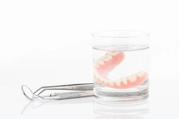 Primer plano de dentaduras en vaso de agua y herramienta dental con noti — Foto de Stock