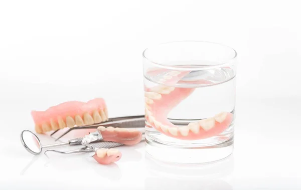 Primer plano de dentaduras en vaso de agua y espejo higienista dental — Foto de Stock