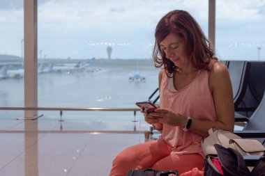 Gitmeden önce havaalanında cep telefonuna bakan bir kadın.