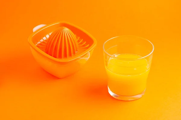 Glas Orangensaft und Entsafter auf orangefarbenem Hintergrund — Stockfoto