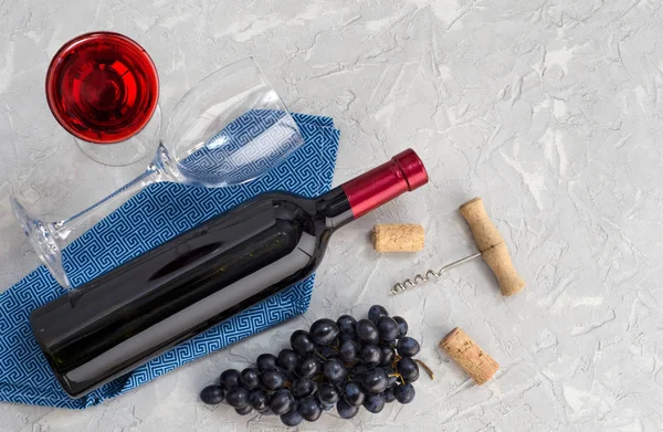 Bottle of wine, wine glass, grapes and corkscrew on gray table.
