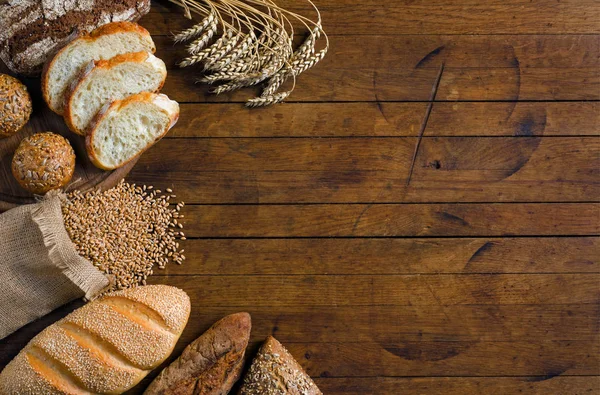 Assortment of bread, ears and grains of wheat on wooden table with copy space for your text. Rustic style, top view.