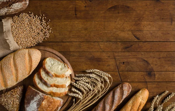 Assortment of bread, ears and grains of wheat in bag on wooden table with copy space for your text. Rustic style, top view.