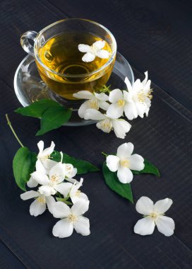 Yasemin çiçekleri ve koyu ahşap arka planda bir bardak çay. Üst görünüm.