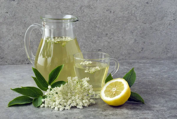Bir sürahi ve gri taş masada limon dilimli mürver çiçeklerinden bir bardak su..