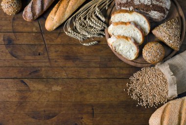 Çeşitli ekmek ürünleri ve ahşap masa üzerinde buğday taneleri olan küçük bir torba ve metin için fotokopi alanı. Kırsal biçim, üst görünüm