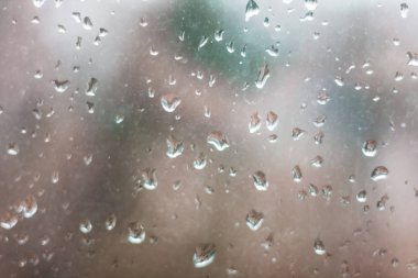 Arka planda yeşil ve kırmızı ağaçla pencereye yağmur damlaları yağar