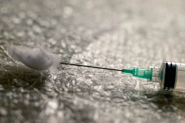 A syringe and a needle with a cotton swab on a polythene with pimples. Virus vaccine