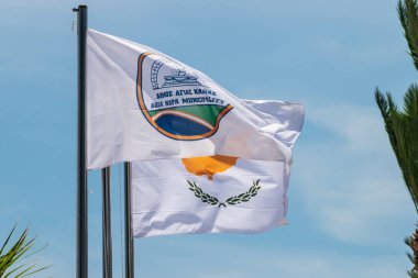 Agia Napa belediyesi bayrağı ve Kıbrıs bayrağı. Bayrak direğinde ve sokak lambasında bayraklar var. Rüzgar bayrağı şişiriyor.