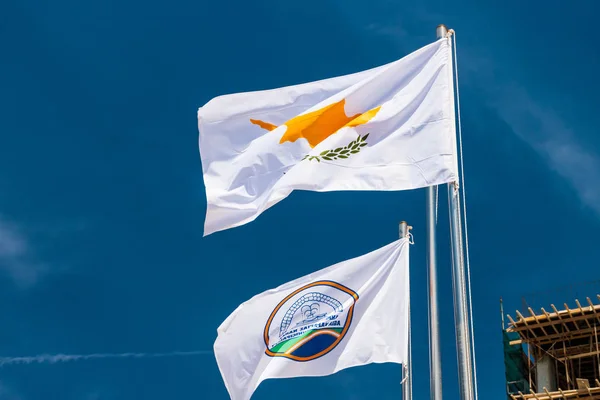 De vlag van de gemeente Agia Napa en die van Cyprus. Vlaggen op de vlaggenmast en de stereet lantaarnpaal. De wind blaast de vlag op. — Stockfoto