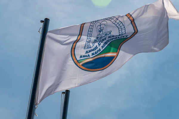 Vlajka obce Agia Napa. Vlajka na stožáru a na sloupu stereetové lampy. Vítr nafoukne vlajku. — Stock fotografie
