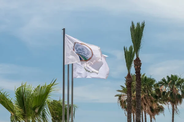 De vlag van de gemeente Agia Napa en die van Cyprus. Vlaggen op de vlaggenmast en de stereet lantaarnpaal. De wind blaast de vlag op. — Stockfoto