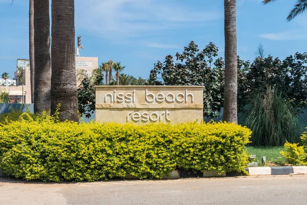 Agia Napa, Kıbrıs - 26 Mayıs 2019: Nissi Beach Resort Hotel tabelası, Ayia Napa. Bu işaret palmiye ağaçlarının arka planında çalılıklara asılmış..