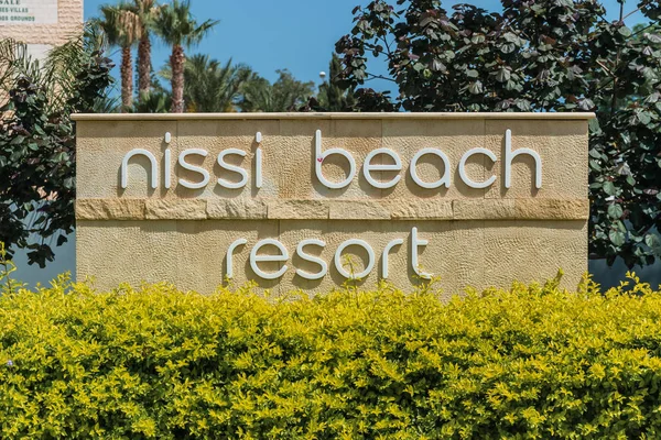 Agia Napa, Kıbrıs - 26 Mayıs 2019: Nissi Beach Resort Hotel tabelası, Ayia Napa. Bu işaret palmiye ağaçlarının arka planında çalılıklara asılmış..