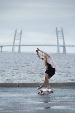 Güzel genç kız onun longboard th yakınındaki yolda sürme