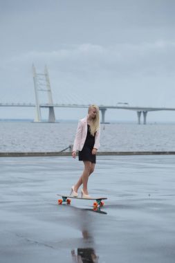 Güzel genç kız onun longboard th yakınındaki yolda sürme