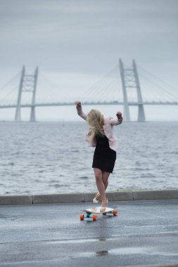 Güzel genç kız onun longboard th yakınındaki yolda sürme