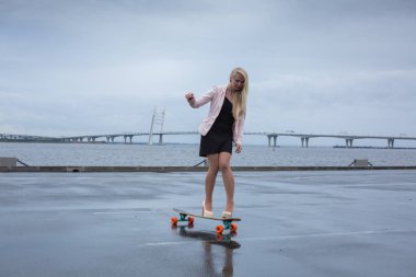 Güzel genç kız onun longboard th yakınındaki yolda sürme